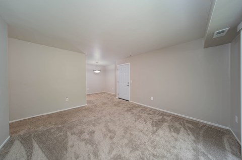 a spacious living room with carpet and a door to a bedroom